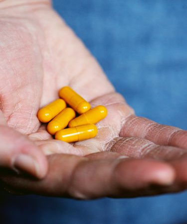 Eine geöffnete Hand hält mehrere gelbe Medikamentenkapseln, die in der Handfläche liegen.