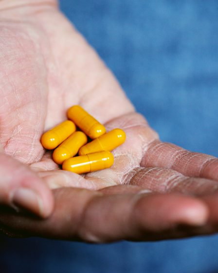 Eine geöffnete Hand hält mehrere gelbe Medikamentenkapseln, die in der Handfläche liegen.