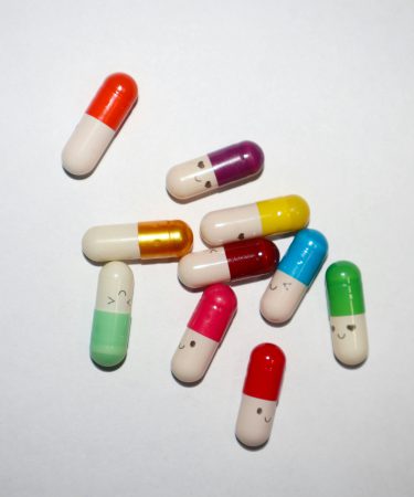 Mehrere bunte Medikamentenkapseln mit verschiedenen Farben liegen verstreut auf einem weißen Hintergrund
