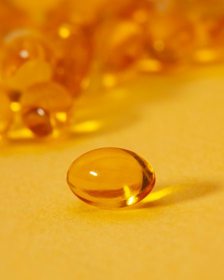 Nahaufnahme einer einzelnen goldenen Weichkapsel auf gelbem Hintergrund mit unscharfen Kapseln im Hintergrund