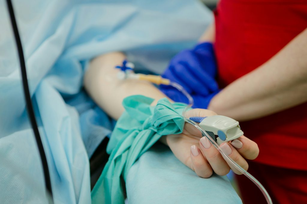 Eine Person liegt auf einer Liege und erhält eine intravenöse Infusion, während medizinisches Personal die Behandlung überwacht.
