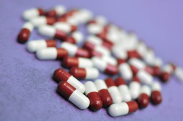 Viele rot-weiße Kapseln liegen verstreut auf einer violetten Oberfläche.