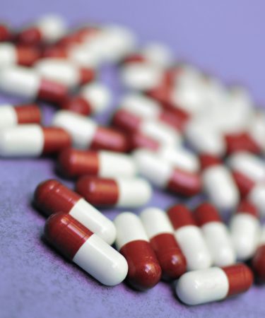 Viele rot-weiße Kapseln liegen verstreut auf einer violetten Oberfläche.