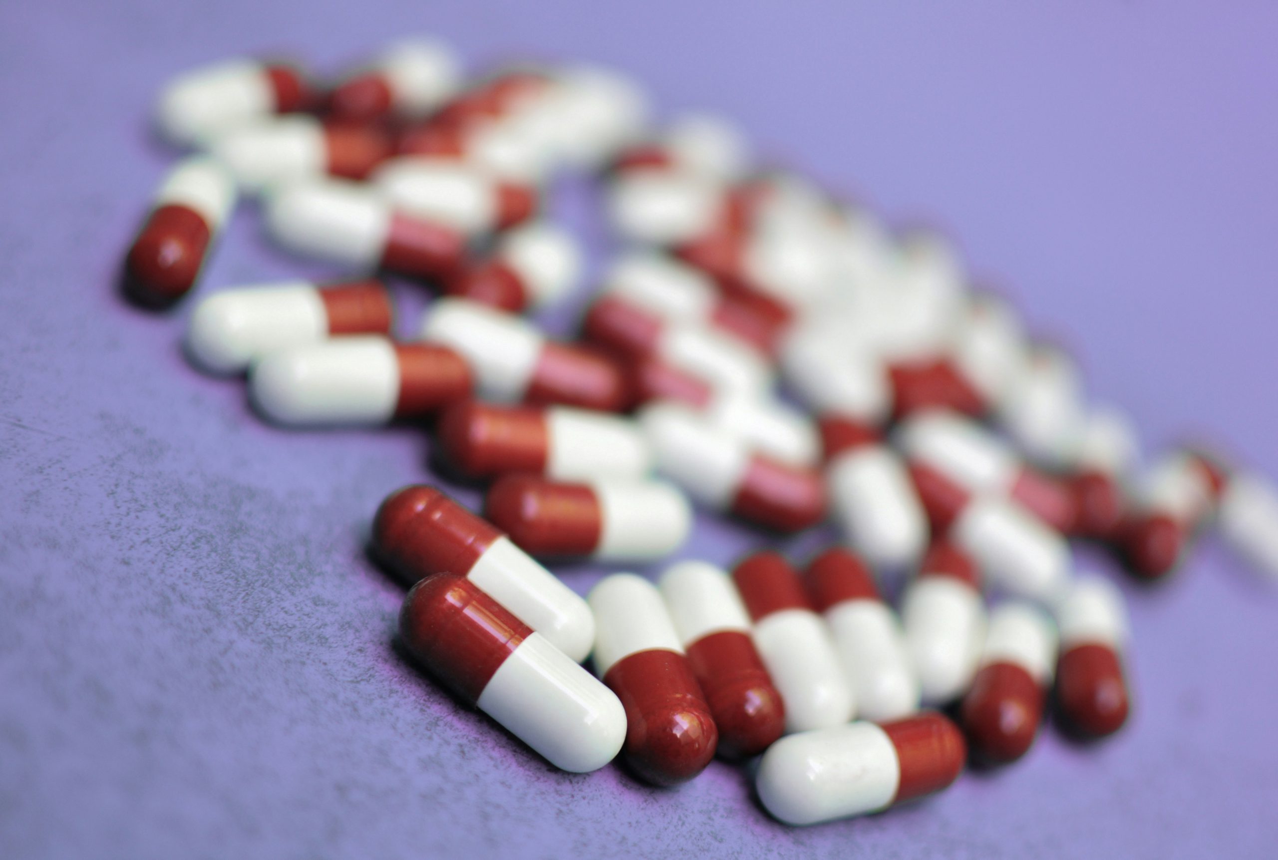 Viele rot-weiße Kapseln liegen verstreut auf einer violetten Oberfläche.