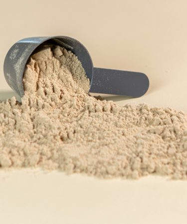 Ein grauer Messlöffel mit feinem, hellbeige Aminosäuren-Pulver auf neutralem Hintergrund – biologischer Schutz vor Wassereinlagerungen.