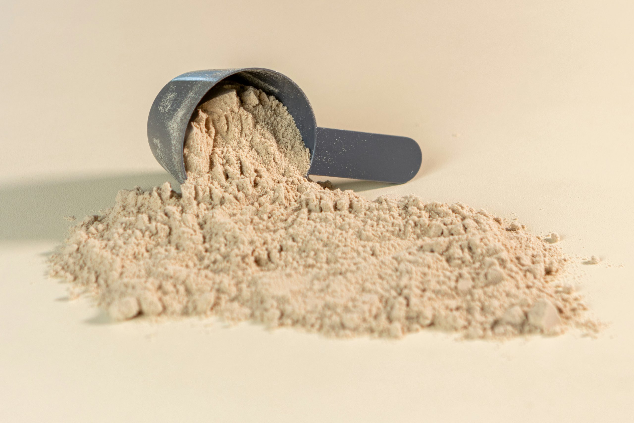 Ein grauer Messlöffel mit feinem, hellbeige Aminosäuren-Pulver auf neutralem Hintergrund – biologischer Schutz vor Wassereinlagerungen.