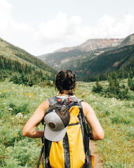 Frau mit gelbem Trekkingrucksack auf einem Bergpfad blickt in ein grünes Tal – aktive Regeneration nach einer Outdoor-Verletzung mit NL-BPC-157.